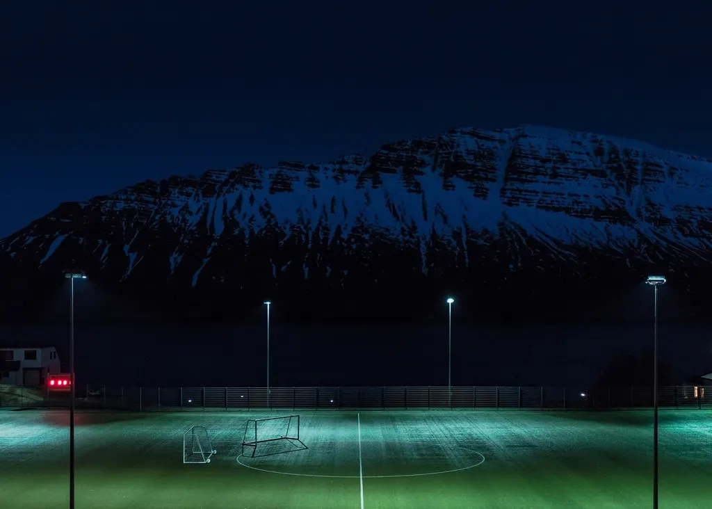 Campo de juego iluminado por focos durante la noche con una ladera nevada al fondo