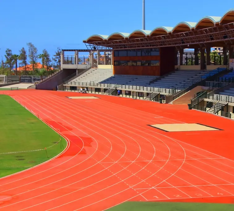 Curva de una pista de atletismo sintética de color rojo con las calles marcadas y una tribuna al fondo