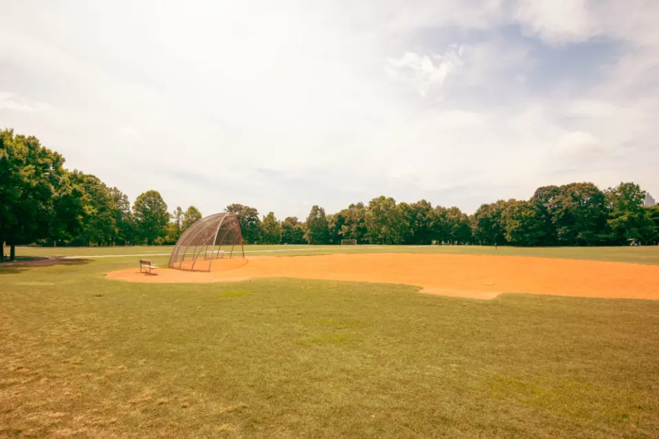 Campo de béisbol vacío con el cuadro interior de tierra batida y la jaula de bateo al fondo