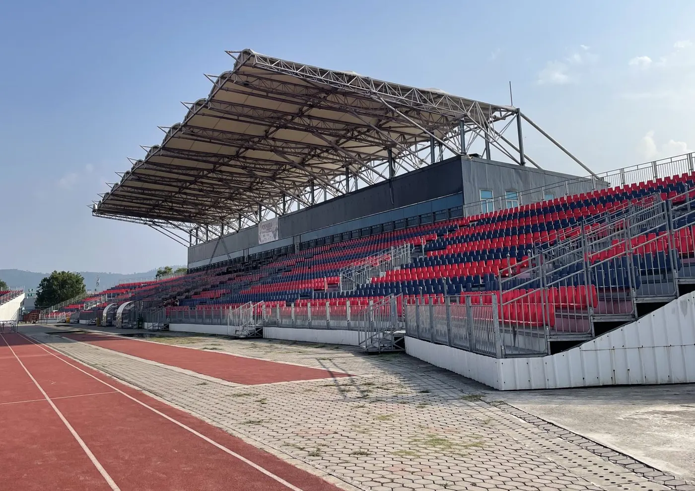 Tribuna cubierta con asientos vacíos junto a una pista de atletismo sintética en un día despejado