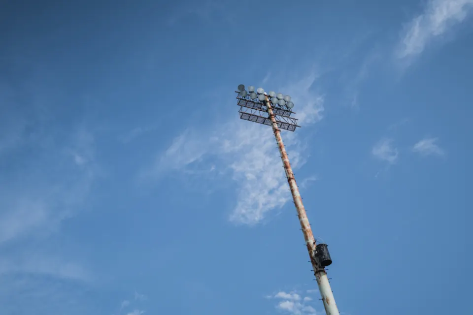 Torre metálica de iluminación deportiva recortada contra un cielo azul con nubes finas
